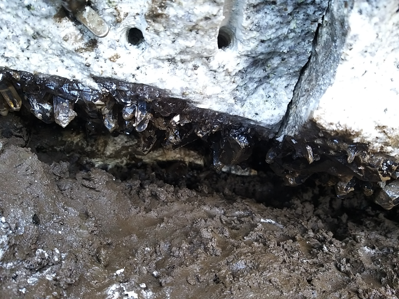 Ein Riss im Granit. An der Decke sind Rauchquarzkristalle und am Boden ist brauner Chloridsand. 